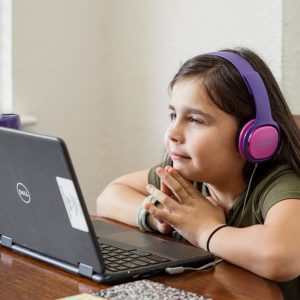 a little girl sitting at a table with a laptop